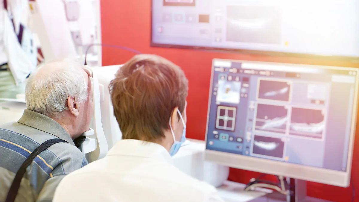A clinician reviewing OCT scans on a monitor beside an older patient