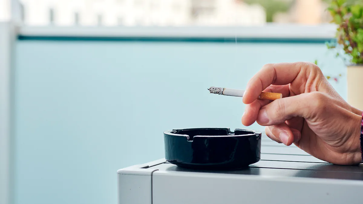A hand holding a lit cigarette over an ashtray