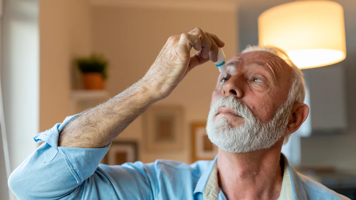 An older man putting in eye drops at home