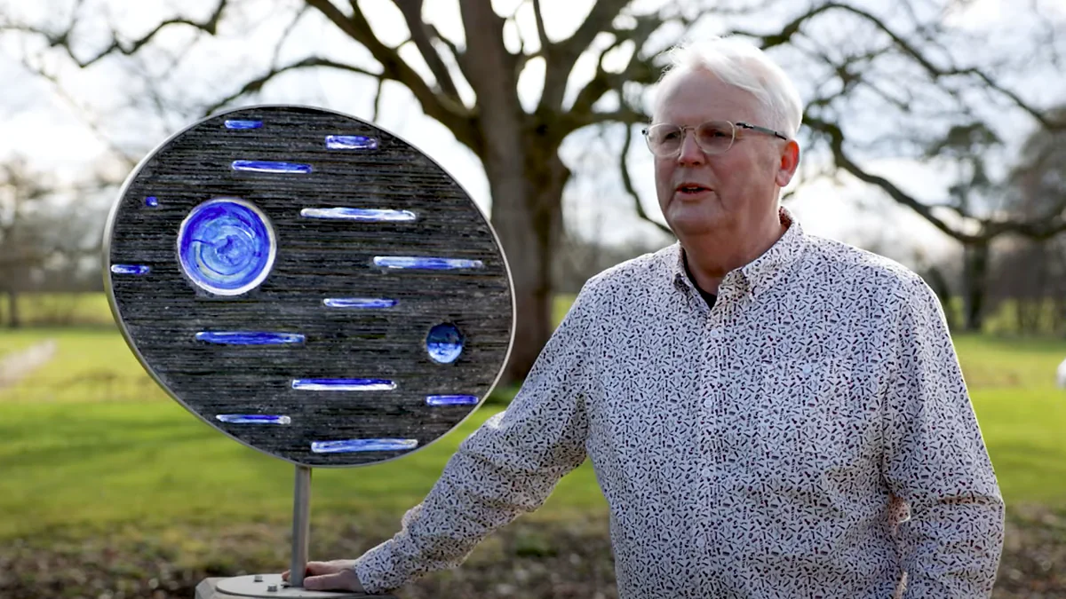 Paul standing beside one of his eye-inspired sculptures in a park
