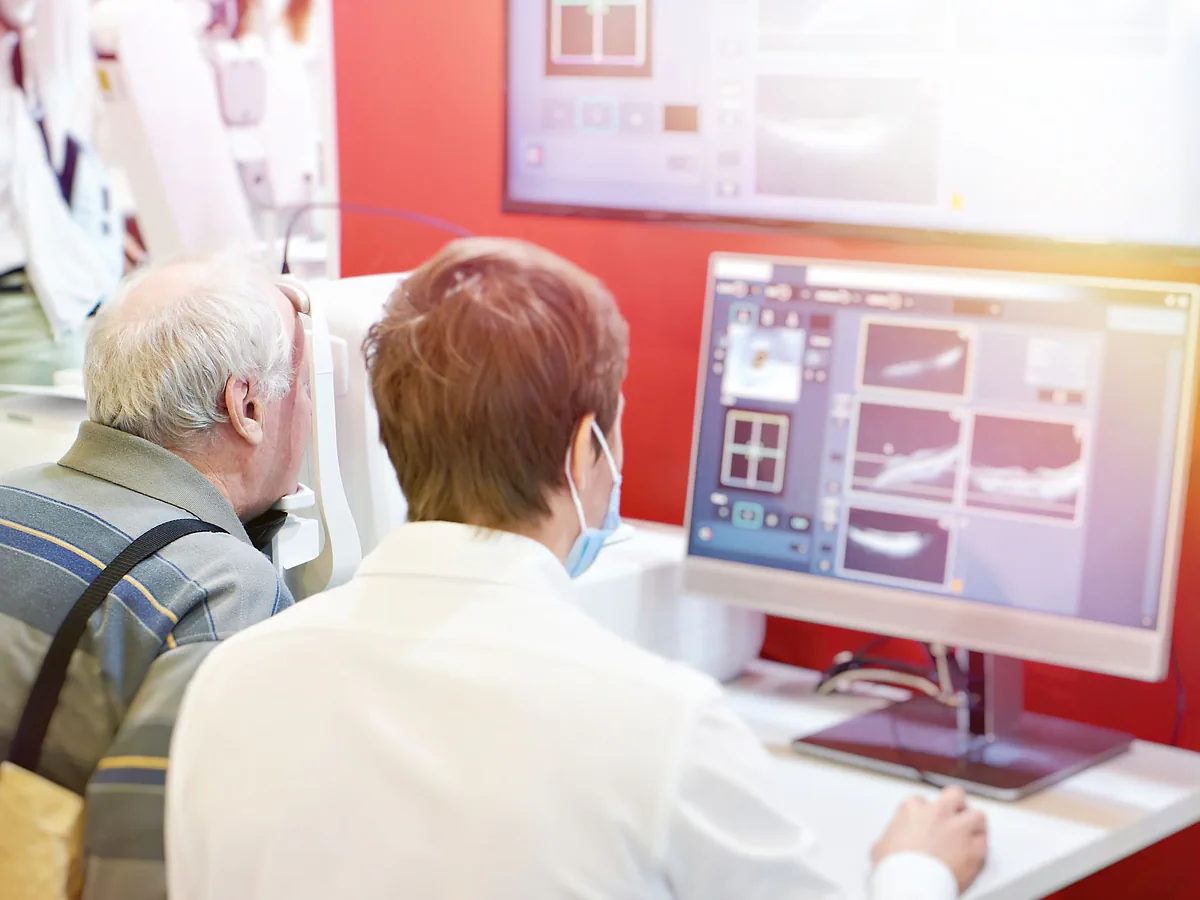 A clinician reviewing OCT scans on a monitor beside an older patient