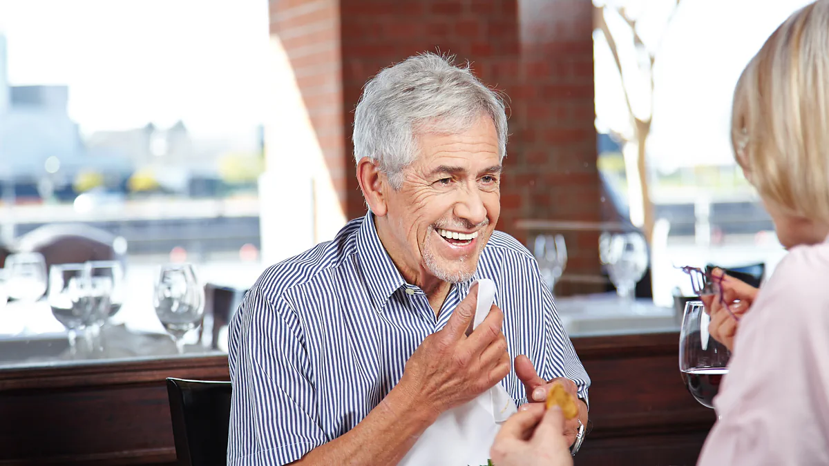 An older man laughing over a meal in a restaurant