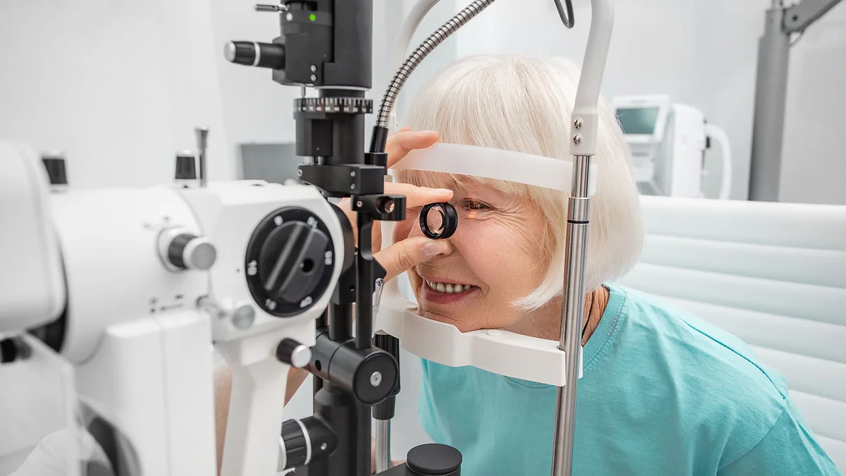 A smiling older woman having her eyes examined at a slit lamp