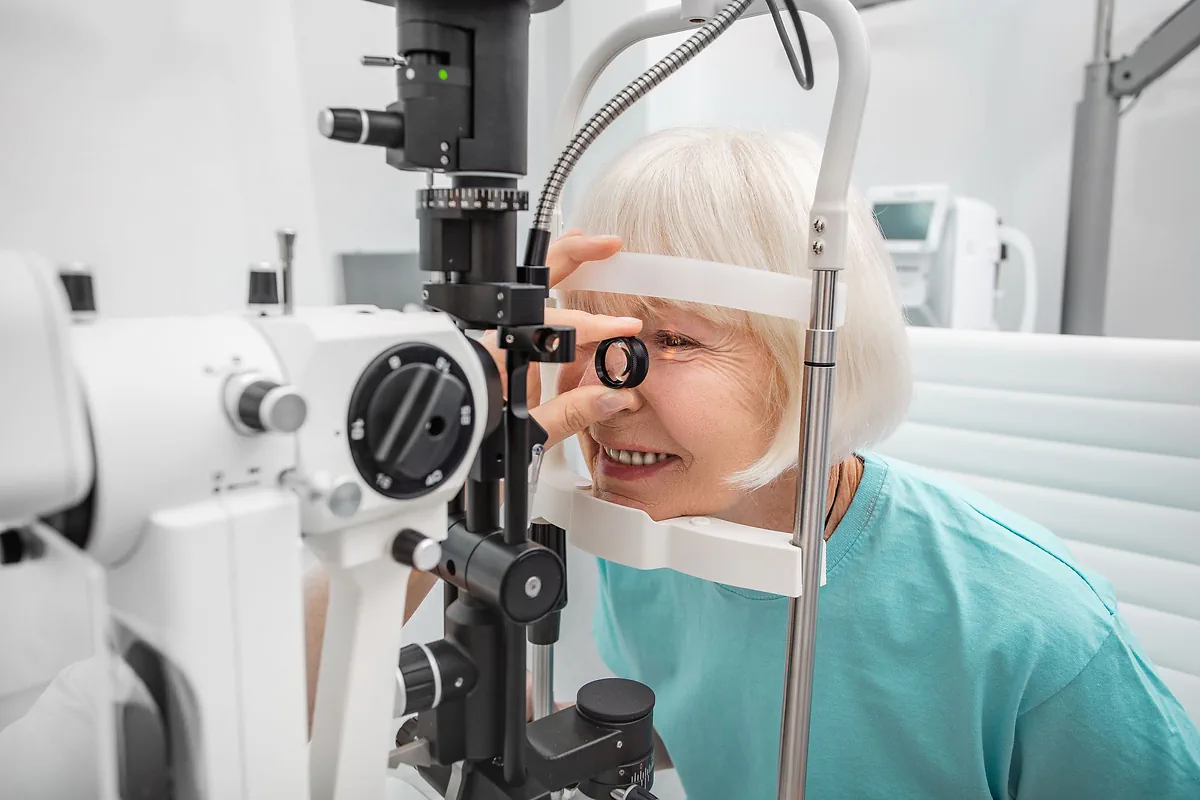A smiling older woman having her eyes examined at a slit lamp