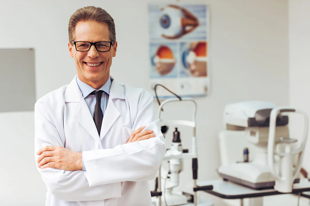 A smiling optometrist with his arms crossed in his consulting room