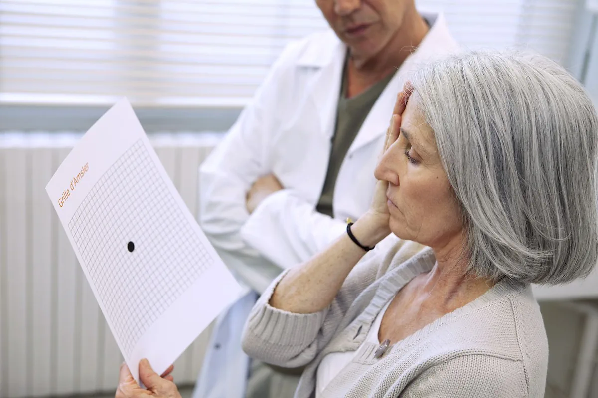 An older woman holding up an Amsler grid while a clinician looks on
