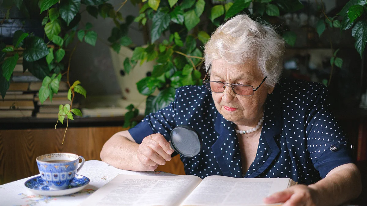 An older woman reading a book with a magnifying glass