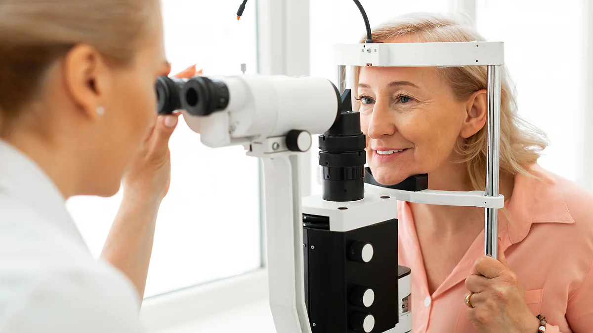 A smiling woman having her eyes examined at a slit lamp