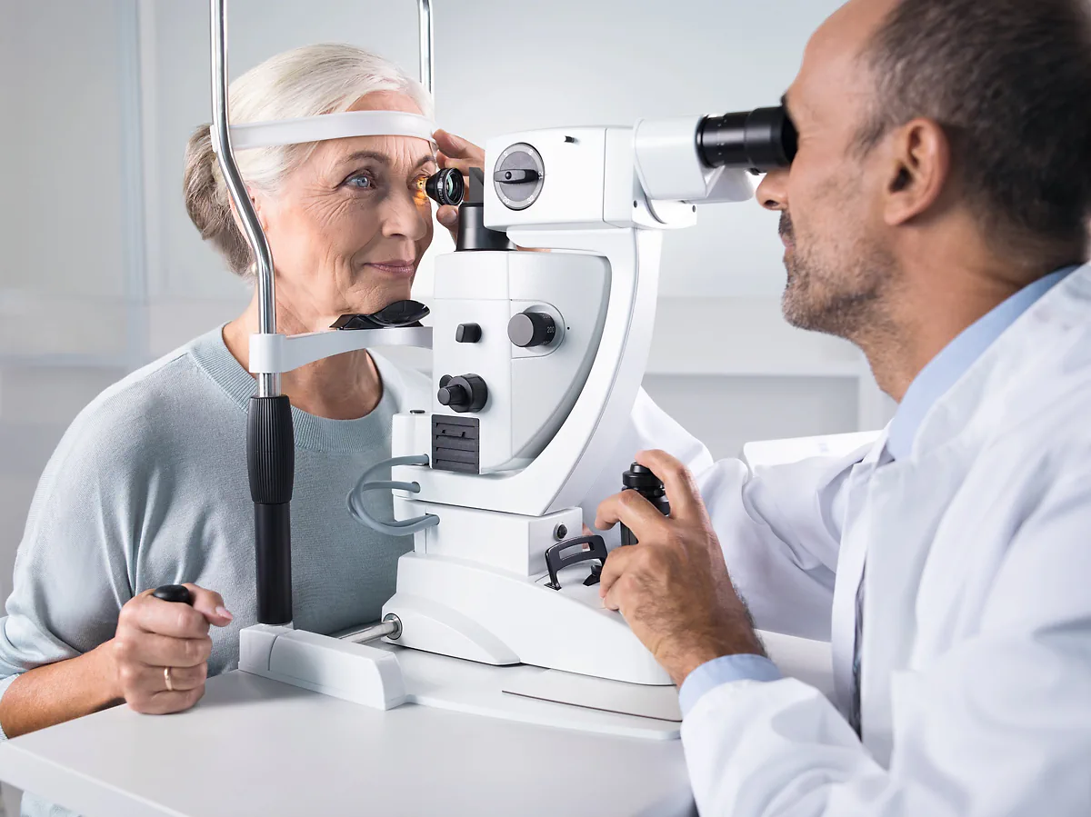 An optometrist performing an eye test with an older woman in a consulting room
